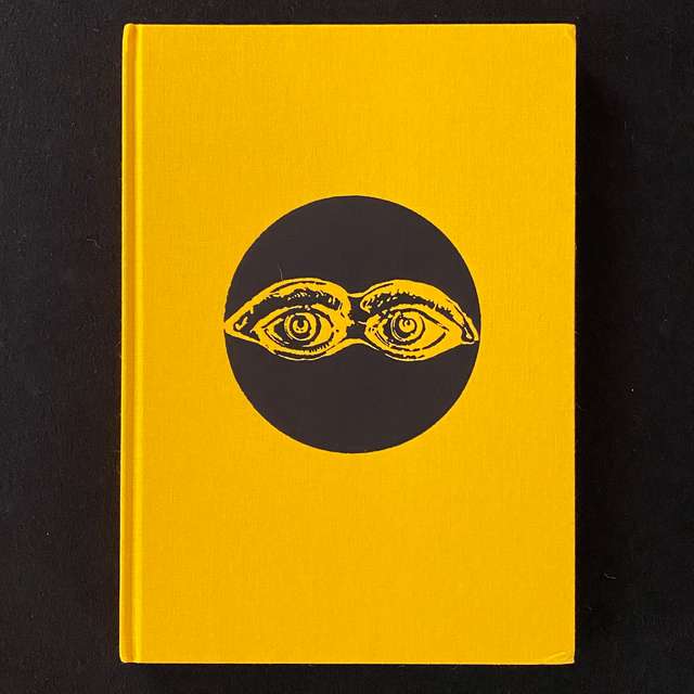 A yellow book with a black circle and some ornamental eyes.