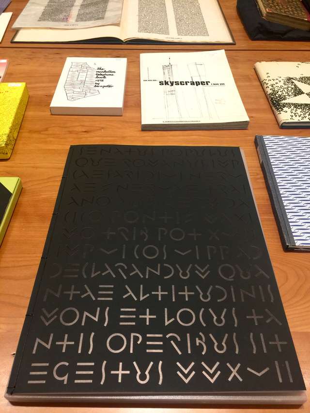 a tables with printed items on it, closest is a large black book with shiny black symbols printed all over the cover