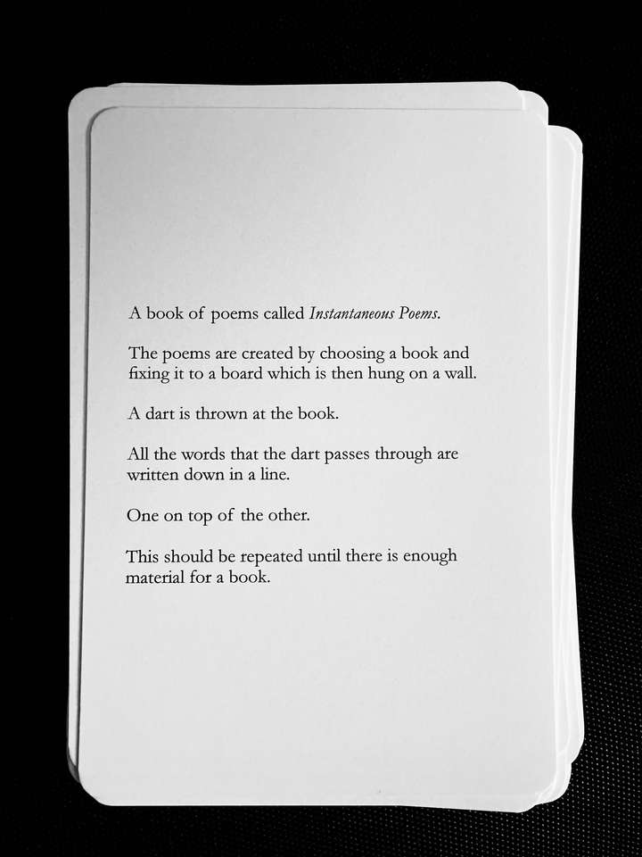 A card saying: A book of poems called Instantaneous Poems. The poems are created by choosing a book and fixing it to a board which is then hung on a wall. A dart is thrown at the book. All the words that the dart passes through are written down in a line. One on top of the other. This should be repeated until there is enough material for a book.